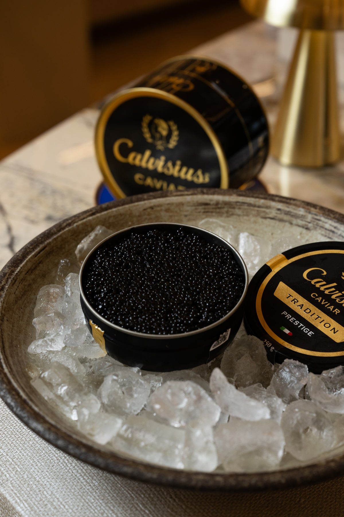 An open tin of black caviar on crushed ice, with closed tins behind it.