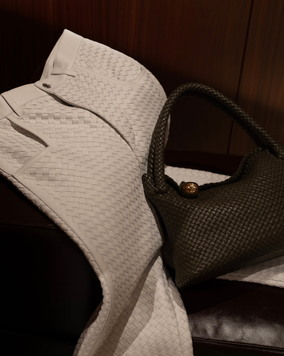 Cream woven trousers draped over a chair beside a dark woven handbag.
