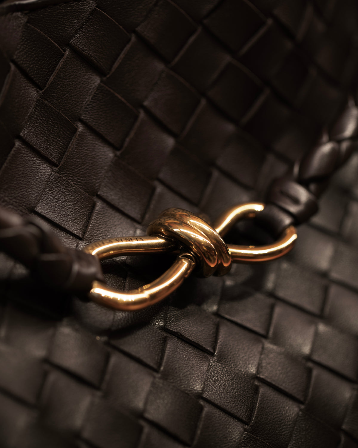 Close-up of a gold-coloured knotted clasp against dark woven leather.