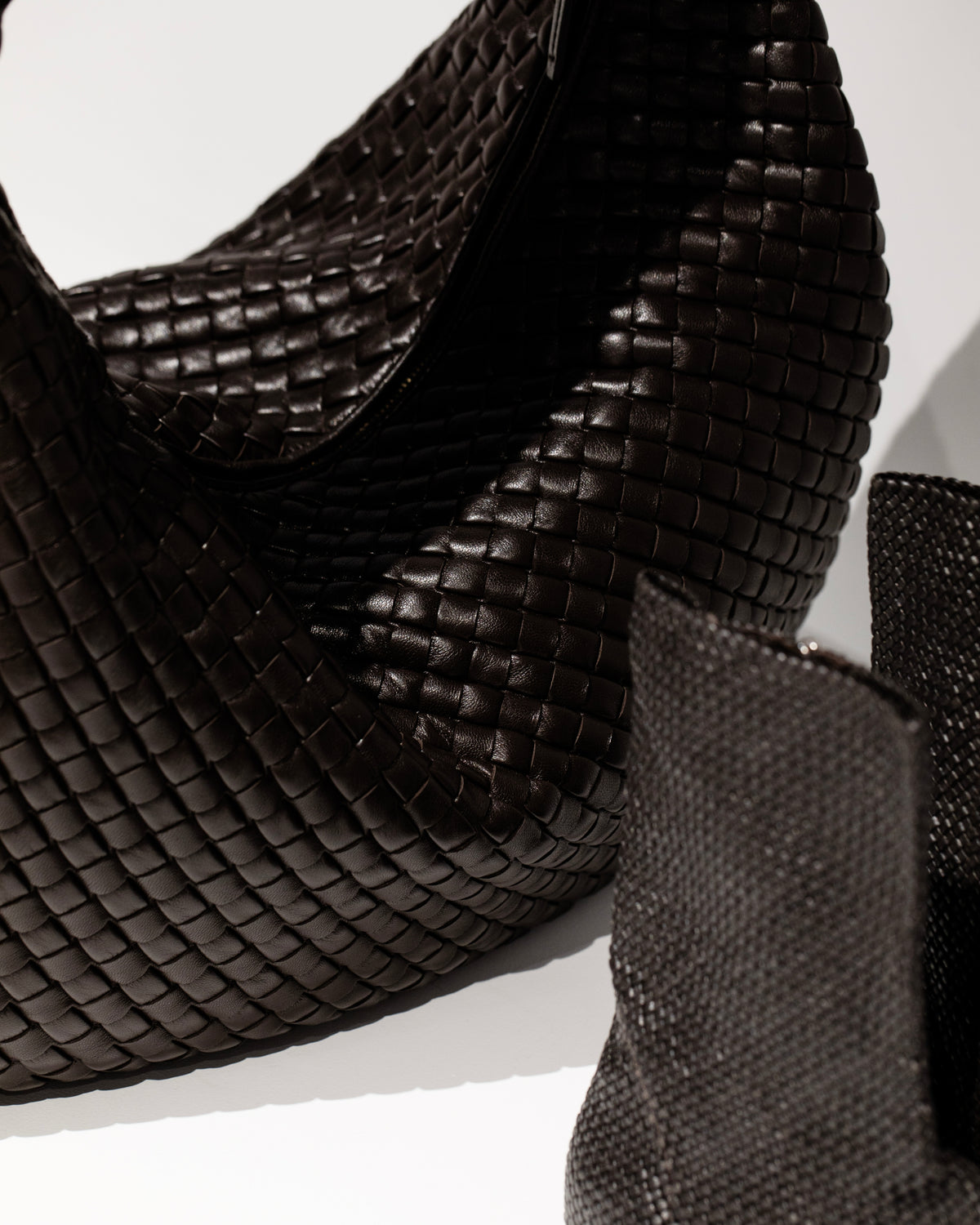 A close view of a dark woven handbag and its curved shoulder strap.
