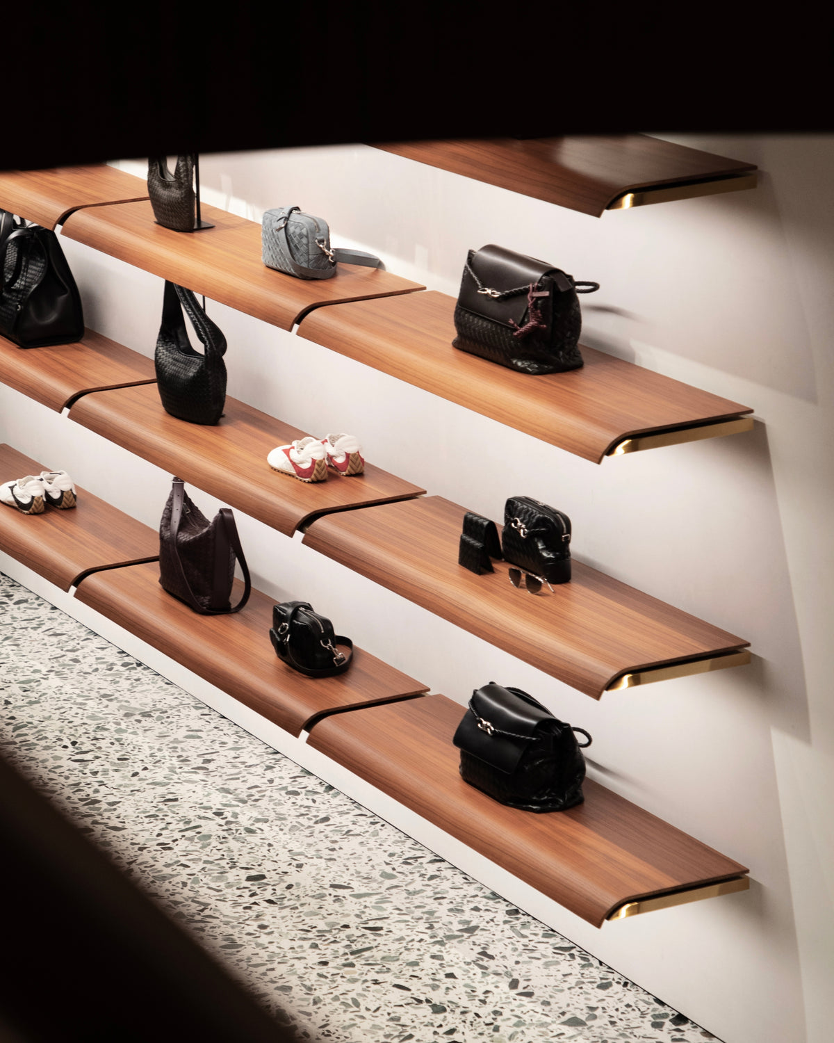 Handbags and shoes arranged across three illuminated wooden display shelves.