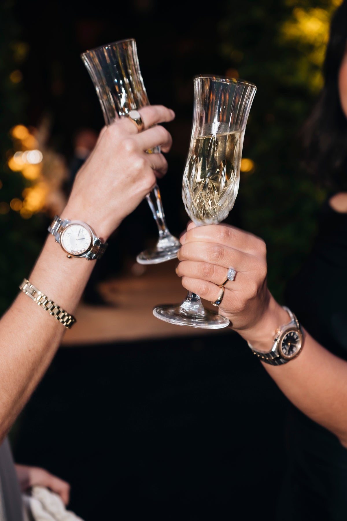 Guests raising champagne flutes, with watches, a bracelet and rings visible.