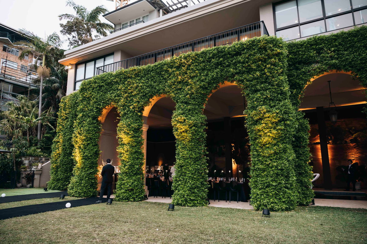 Vine-covered arches opening onto a dining room, viewed across the lawn.