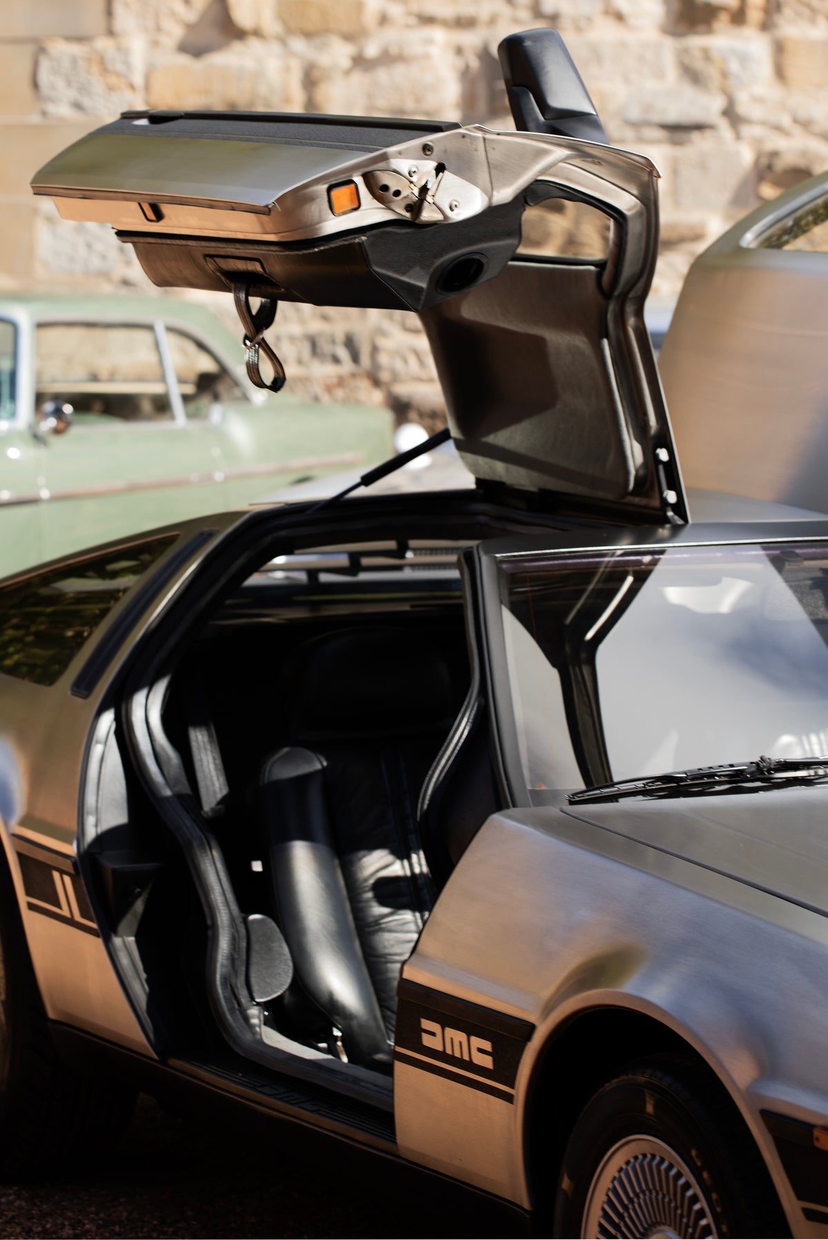 Silver car with its gullwing door raised, revealing a black leather seat.