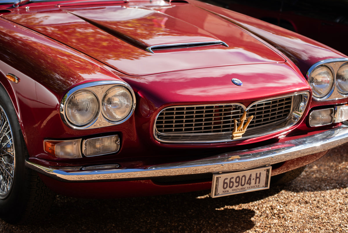 Front of a red car with twin round headlights, a chrome grille and a raised bonnet vent.