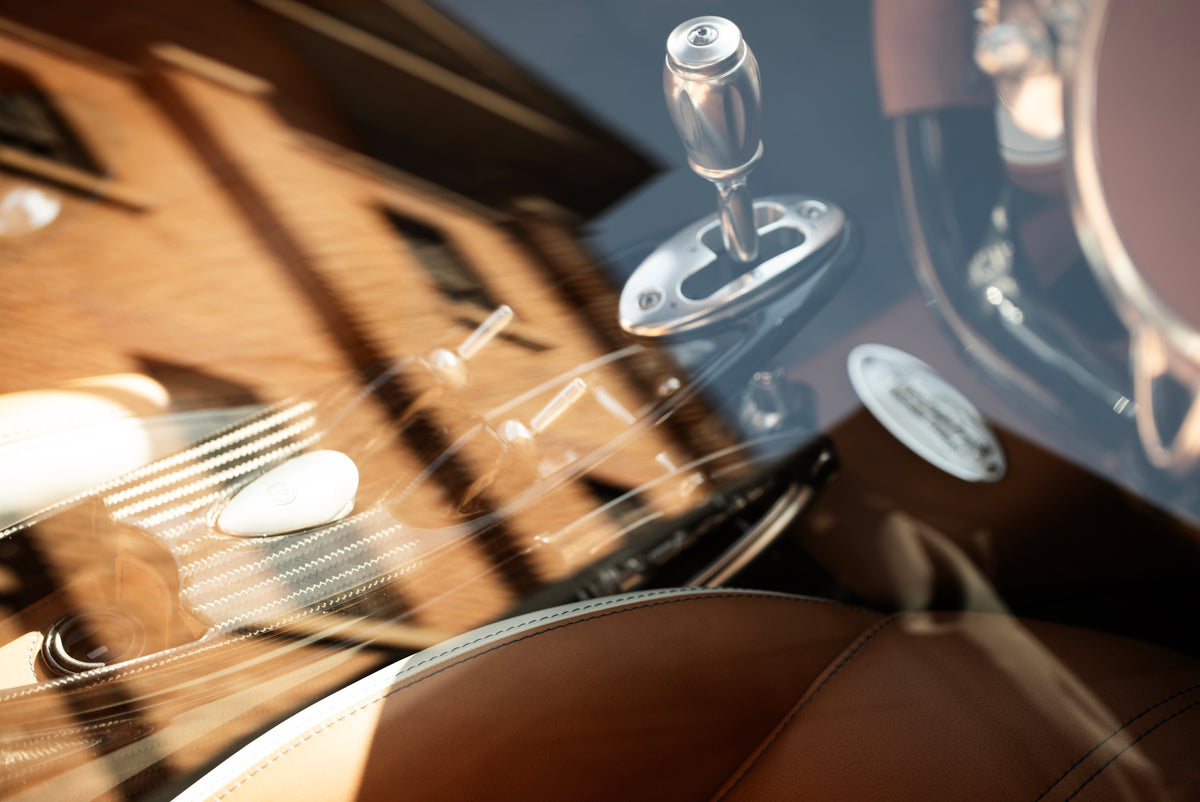 Metal gear lever and tan leather upholstery seen through a car window reflecting a building.