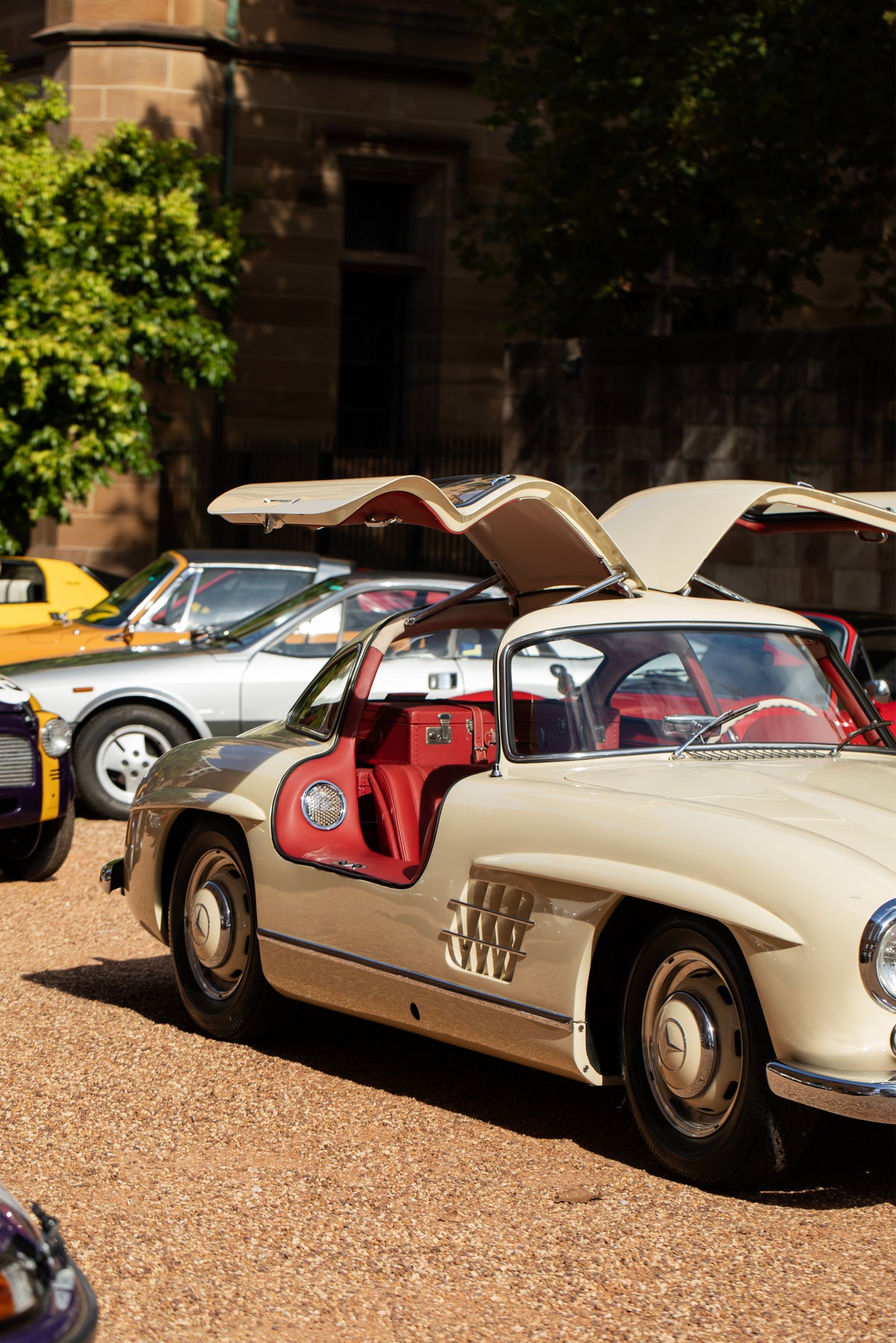 Silver car with raised gullwing doors and red upholstery, parked among other cars.