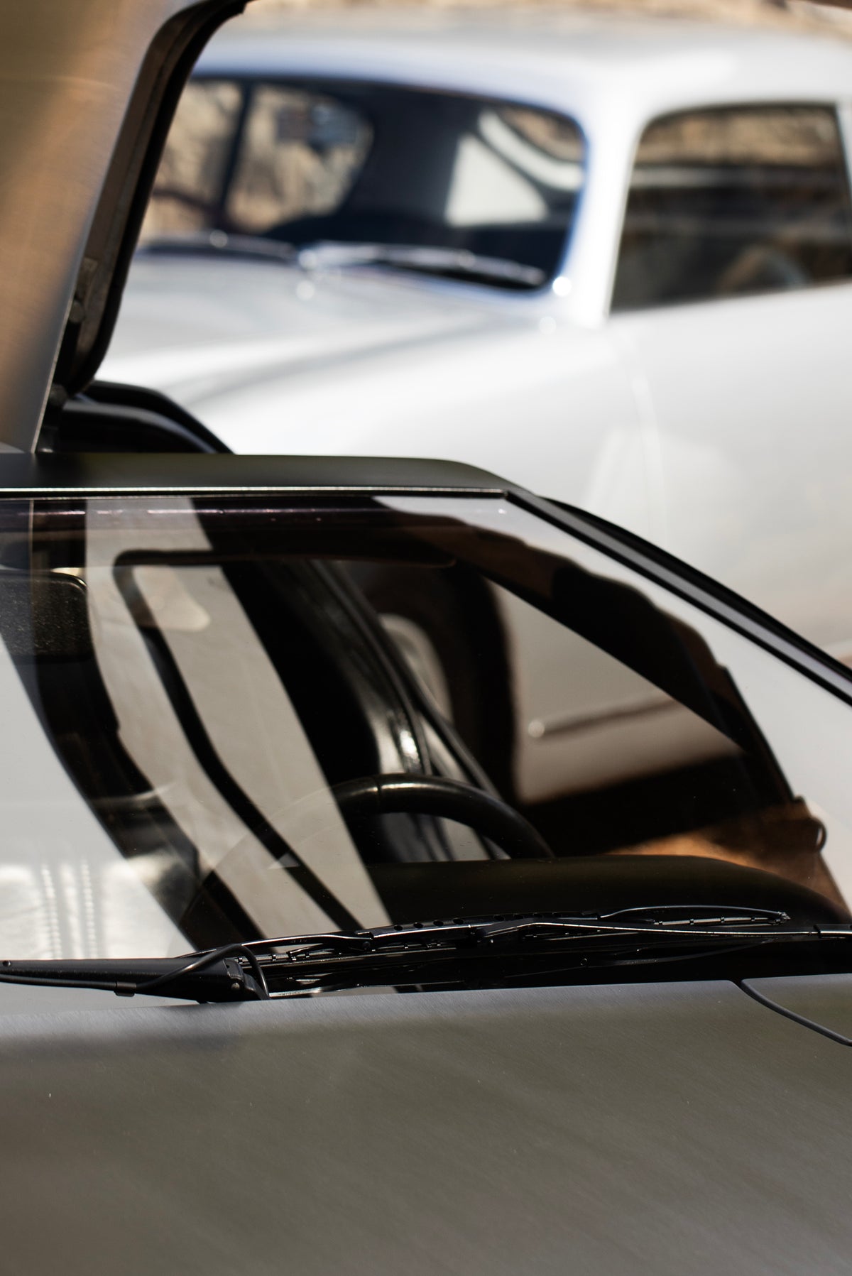 Close view of a silver car's windscreen, with another silver car behind it.