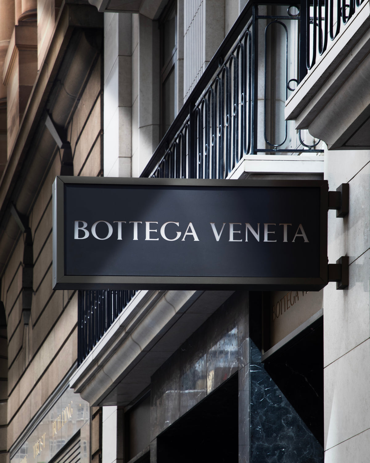 Bottega Veneta sign projecting from a stone shopfront beneath a balcony.
