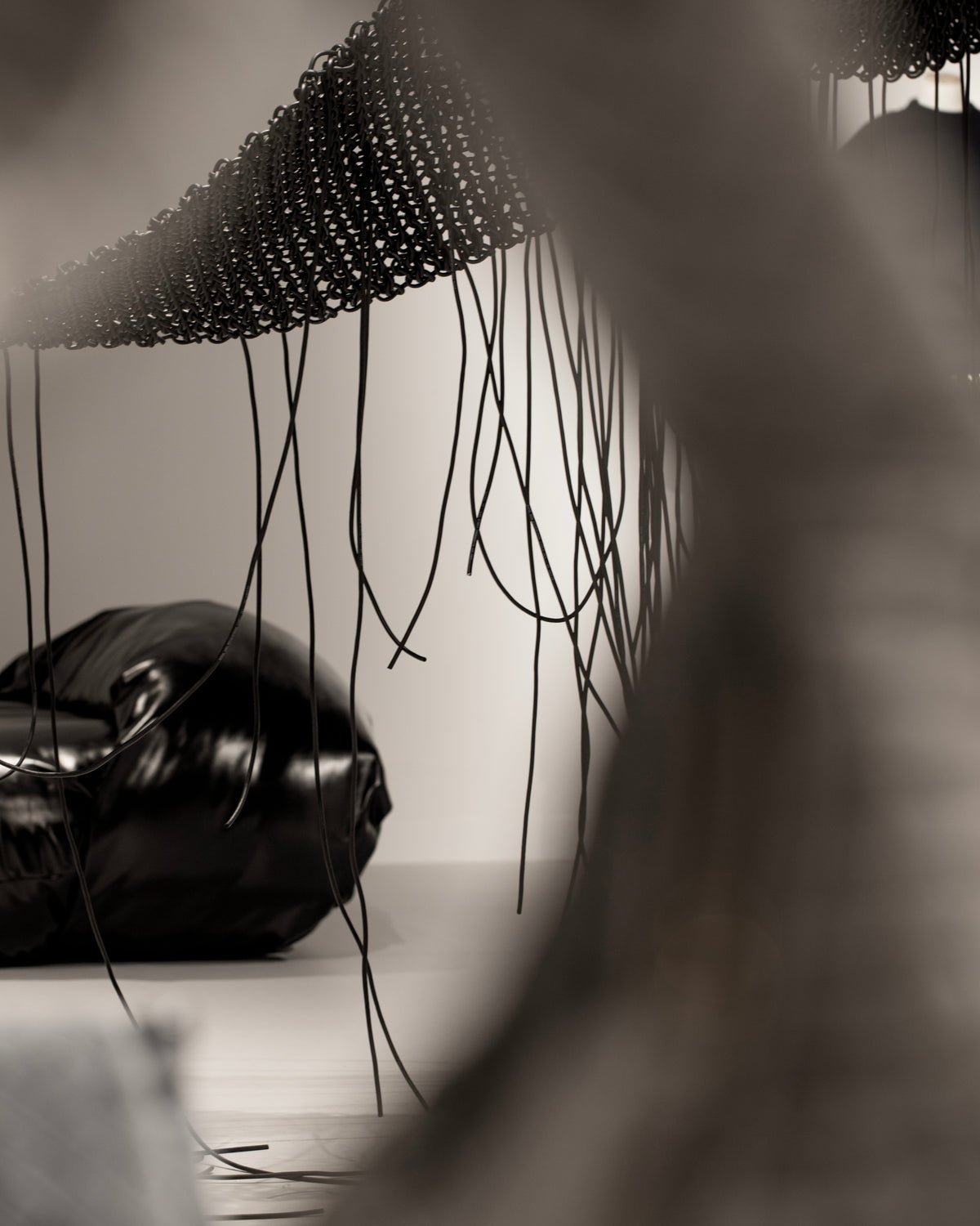 Black-and-white detail of long fringe hanging above a dark handbag.