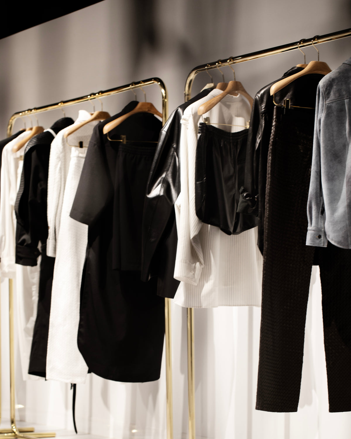 Black and white garments arranged on wooden hangers along brass-coloured clothing rails.