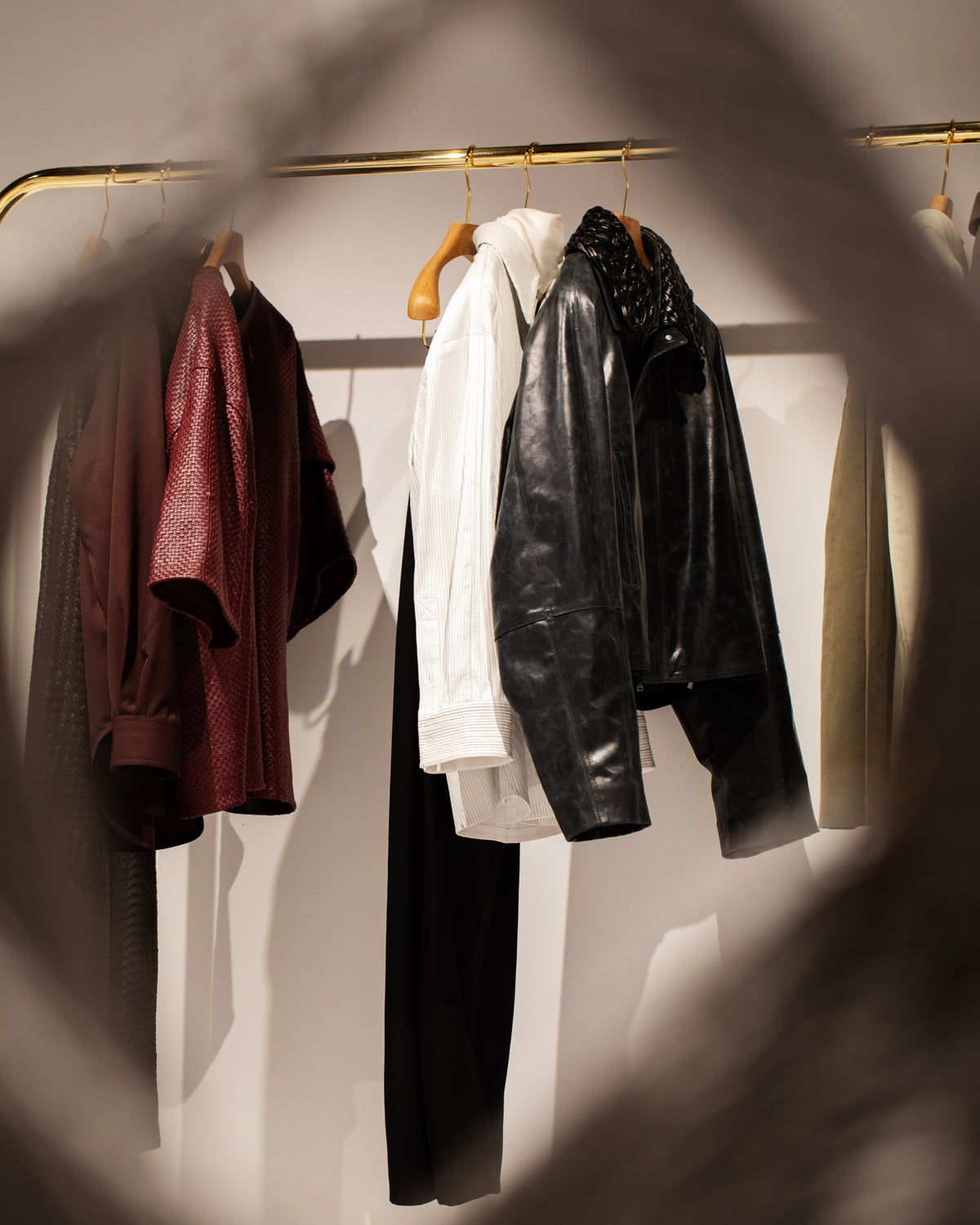 A burgundy top, white shirt and black jacket with trousers hanging on a brass-coloured rail.