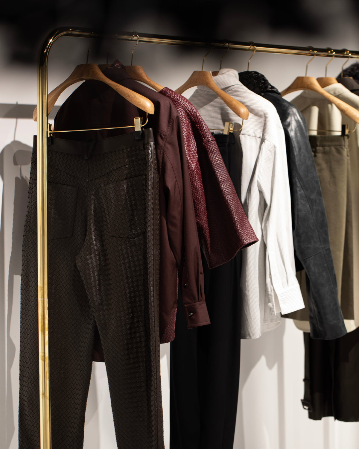 Burgundy, cream and dark garments hanging from wooden hangers on a brass-coloured rail.