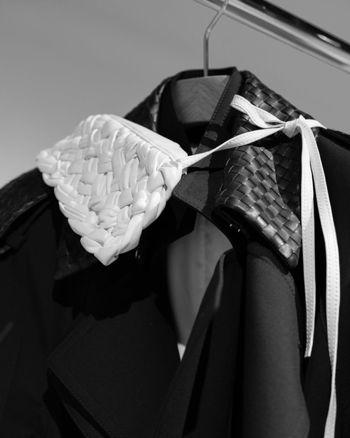 A white woven accessory with long ties draped over a dark garment on a hanger, in black and white.