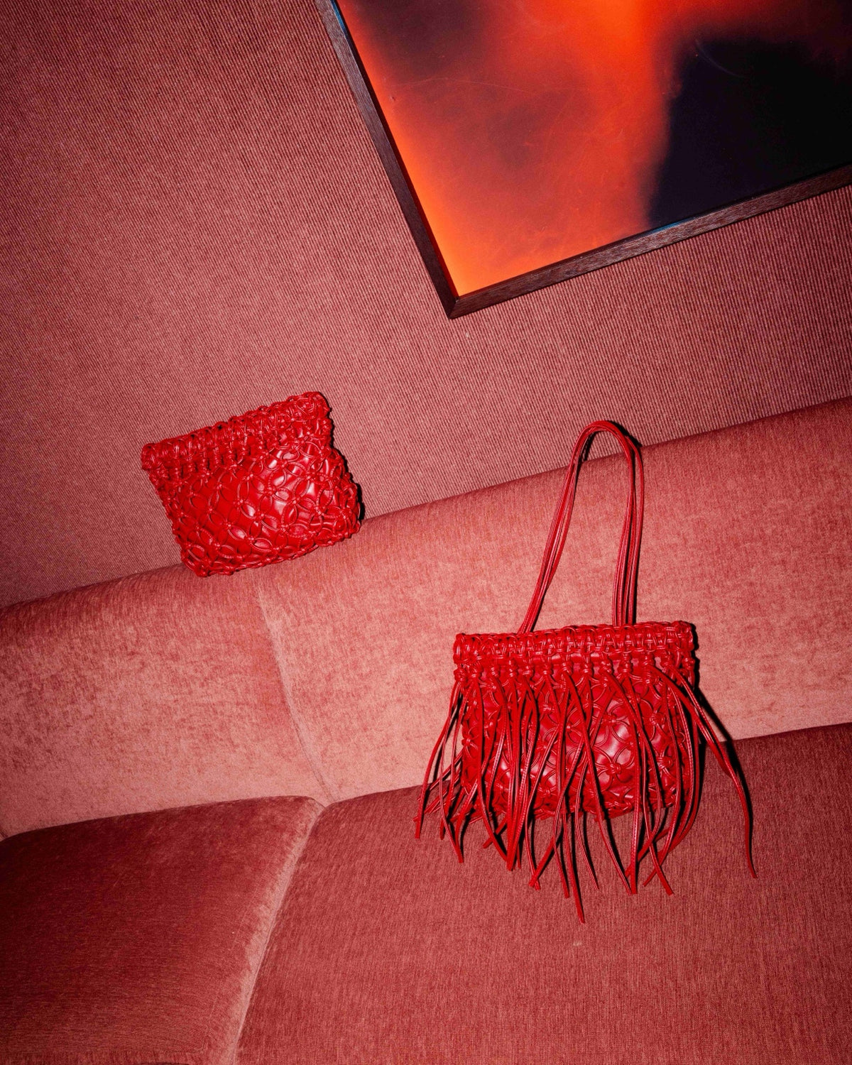 Two red hand-braided A-ESQUE bags on pink upholstery beneath an artwork