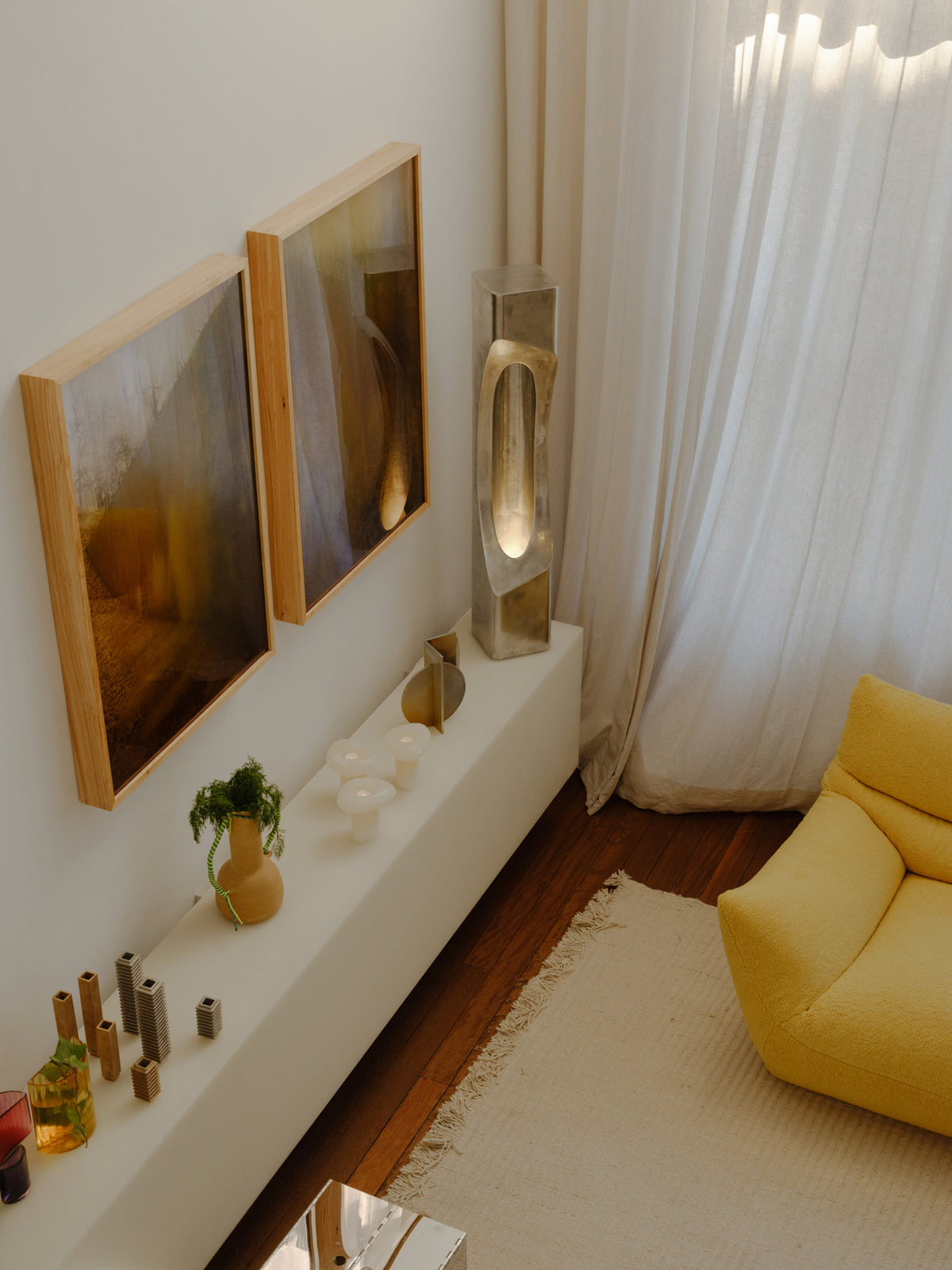Glass objects, metal forms and framed works beside the yellow sofa.
