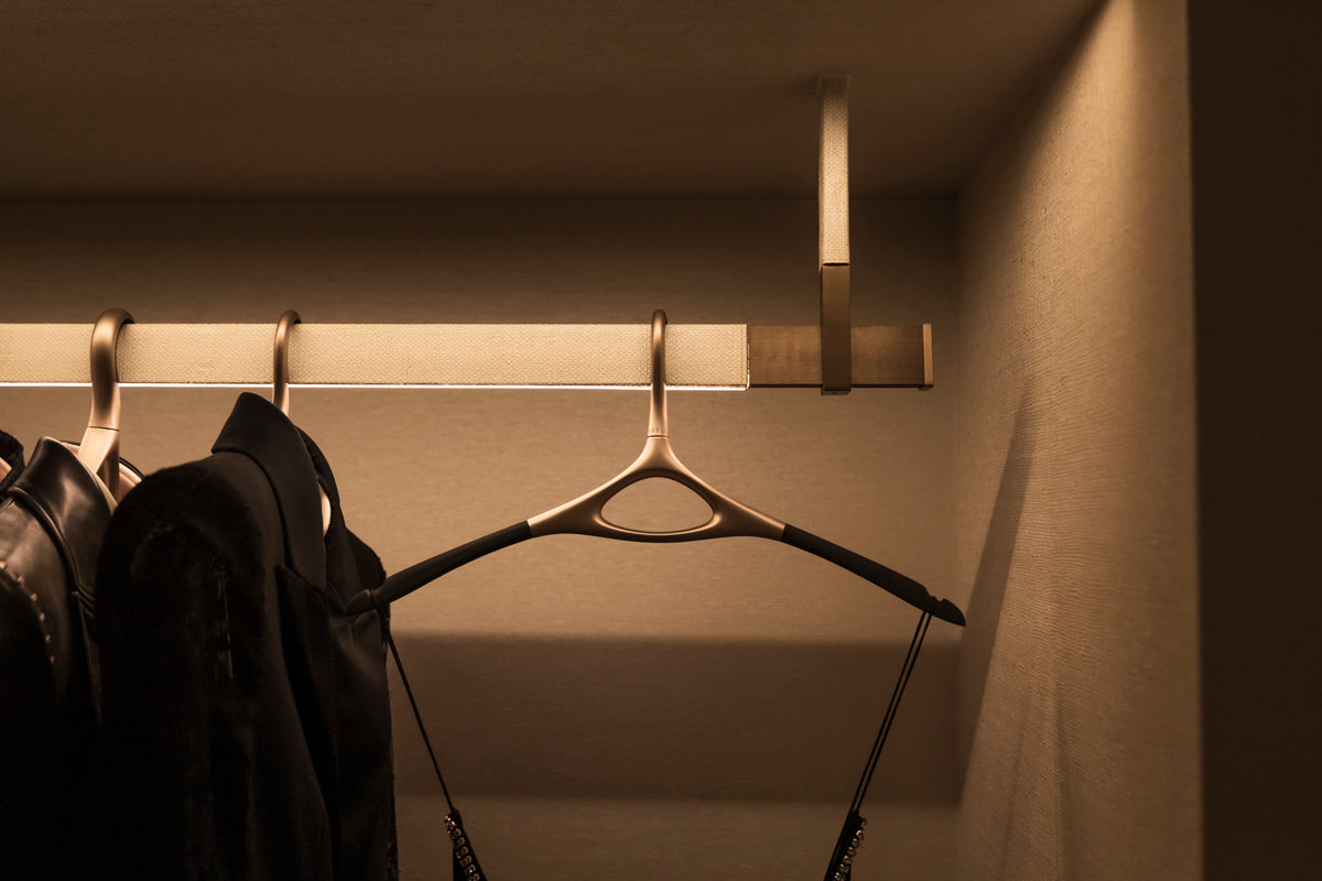 Dark garments on sculptural hangers beneath warm lighting at Three Over Six