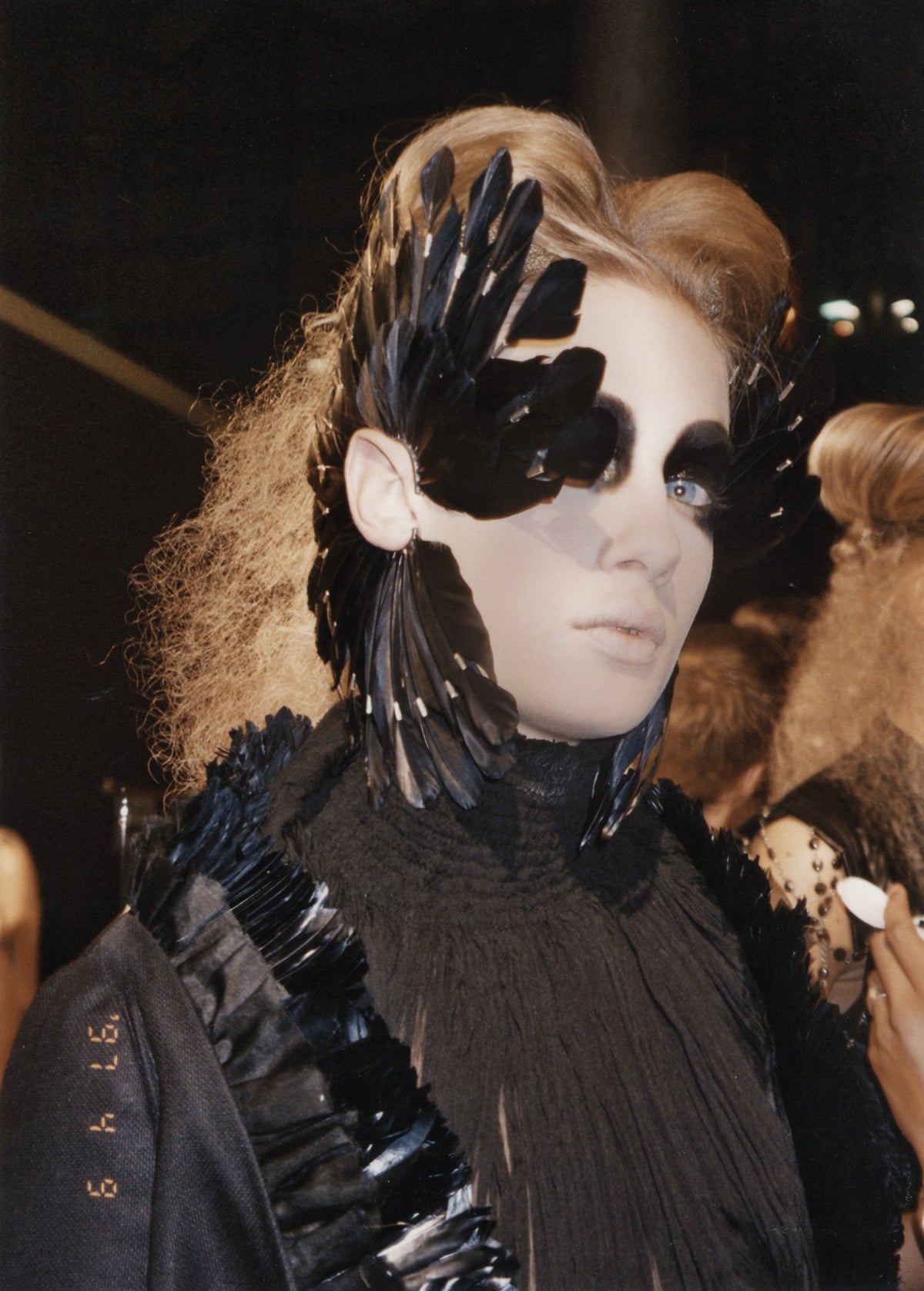 Black-and-white backstage portrait of a model with feathers framing her face, from the Mira Chai-Hyde Alexander McQueen archive.
