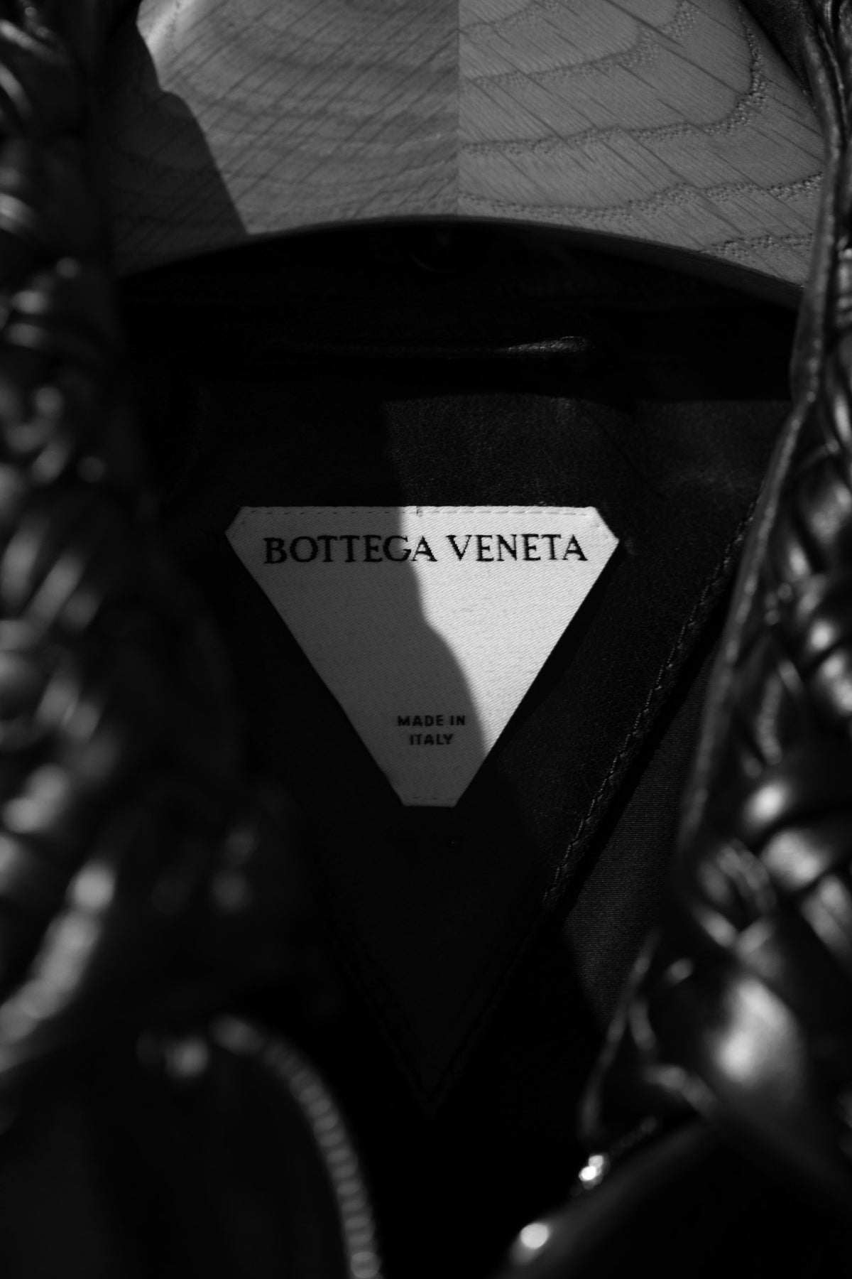 Bottega Veneta garment label beneath a wooden hanger, photographed in black and white