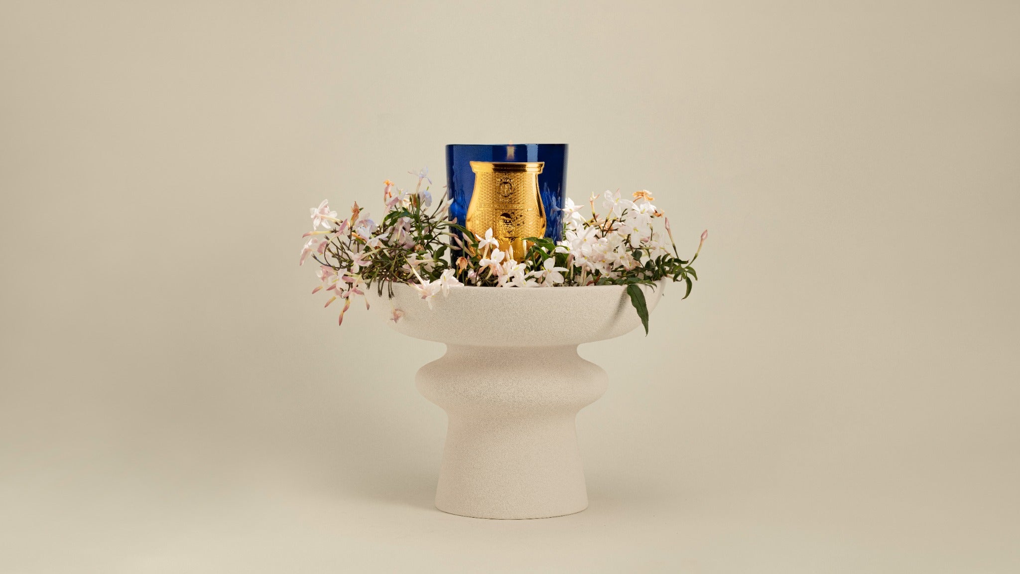 A blue Trudon Madurai candle surrounded by jasmine in a sculptural bowl.