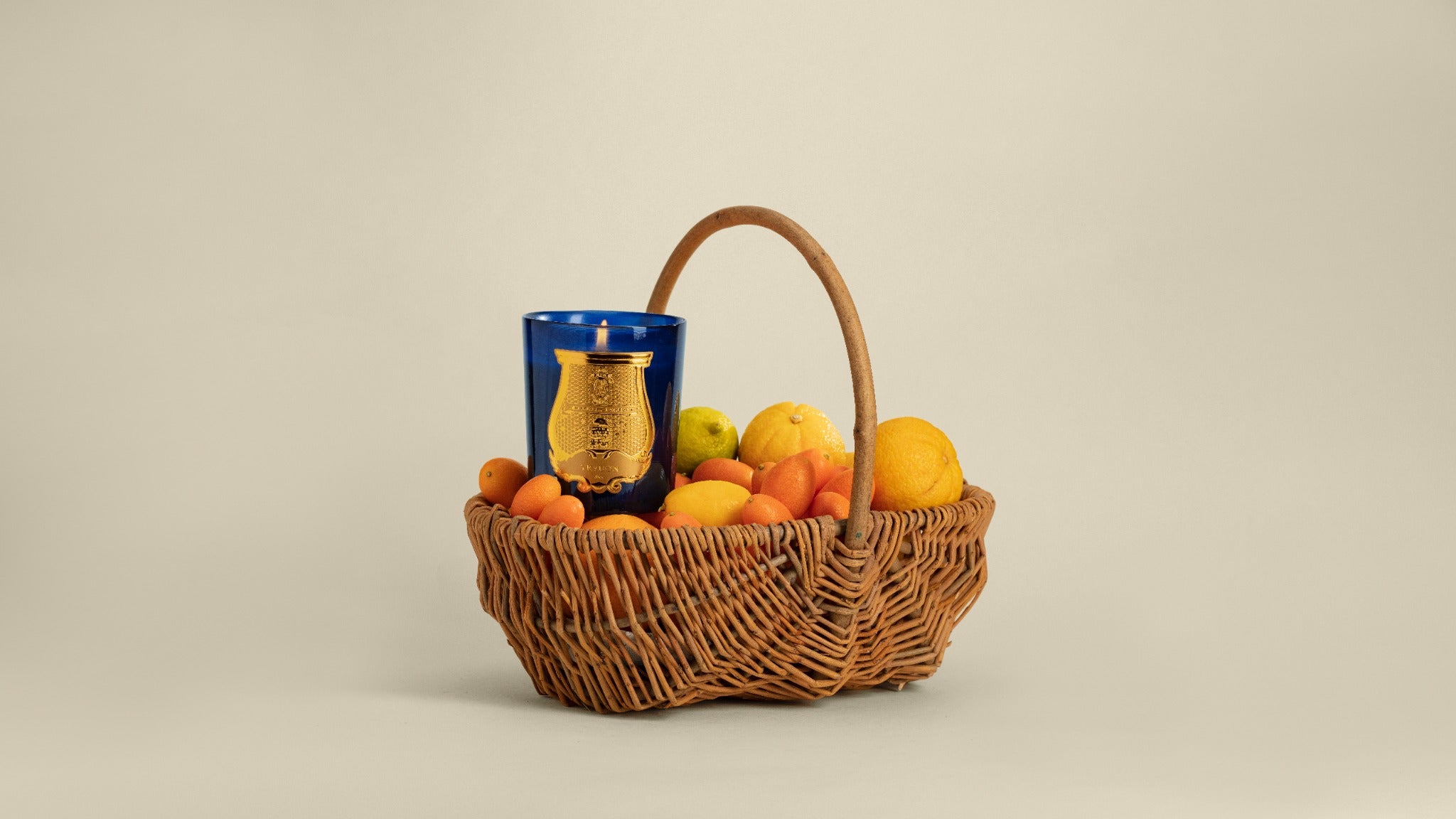 A blue Trudon Reggio candle in a basket of citrus fruit.