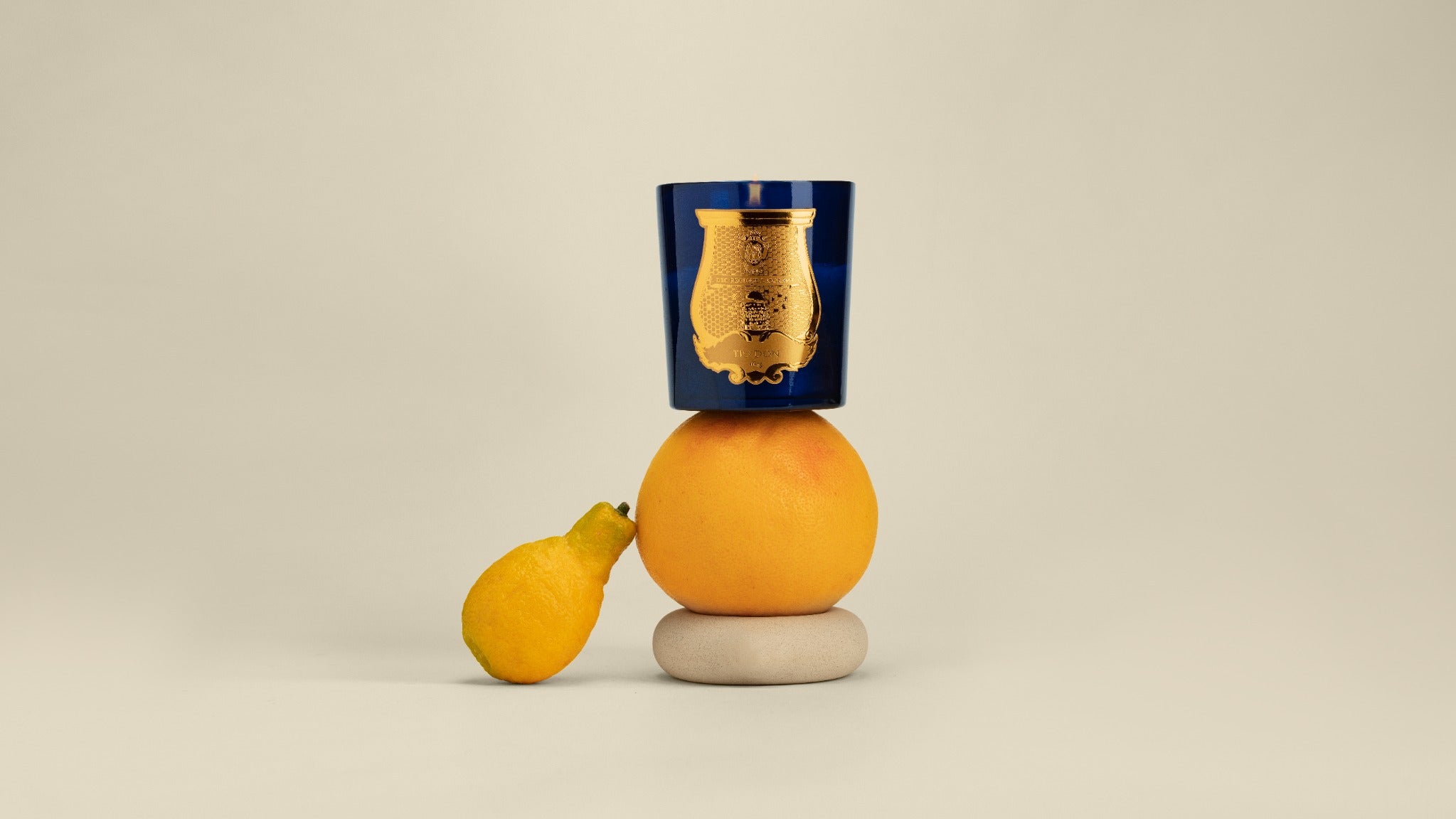 A blue Trudon Salta candle balanced above grapefruit and a pale stone.