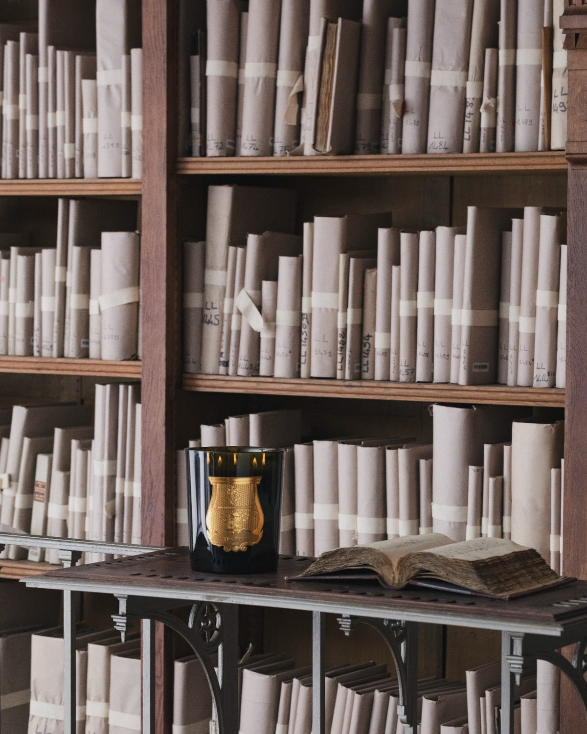 Trudon candle beside an open book in a historic library
